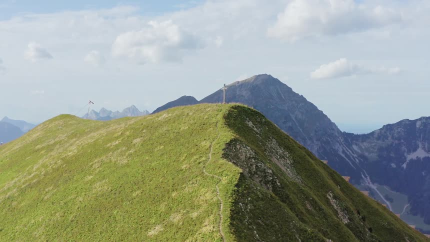 A hill with a cross with mountains and the sky in the background