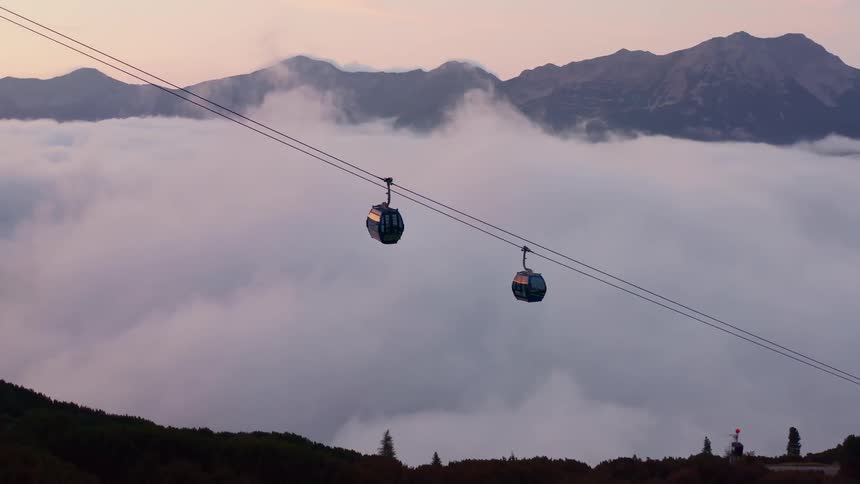 Cable cars going up and down a mountain over clouds