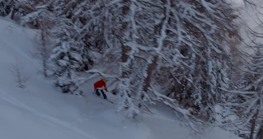 A person as they snowboard down a steep mountain side covered in patches of trees