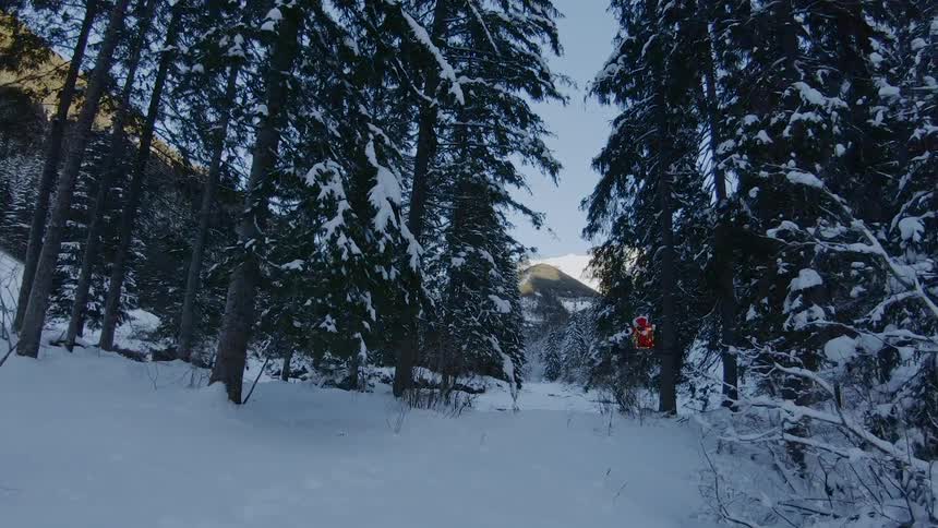 A small flying drone navigates through a snow covered forest full of tall trees