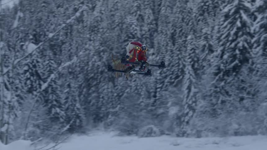 A drone made to look like santa claus and reindeer fly over a snow covered area