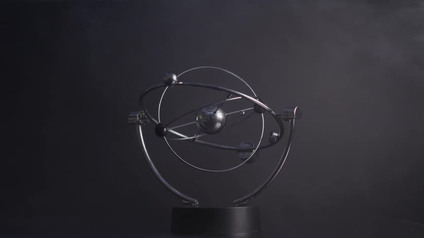 A perpetual motion toy spins back and forth as smoke blows around it
