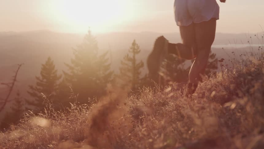 A person wearing jogging shoes and a small pair of shorts runs on a hillside during a sunset