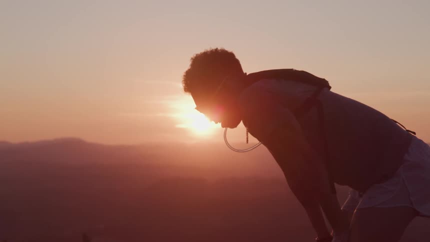 Man bending with hands on thighs outdoors at sunset