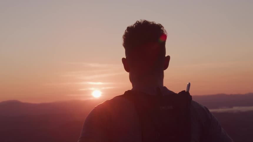 A silhouette shows a man looking across the horizon at sunset