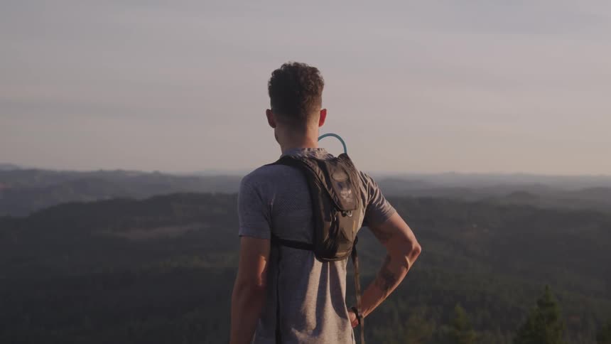 A man wearing a tiny backpack looking out over a forest from high altitude