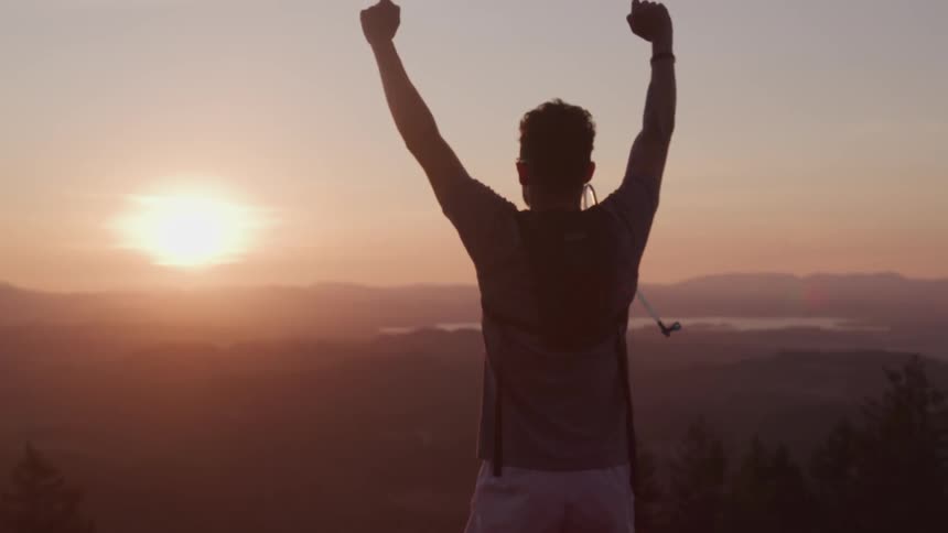 Man runs uphill and raises hands in victory gesture at sunset