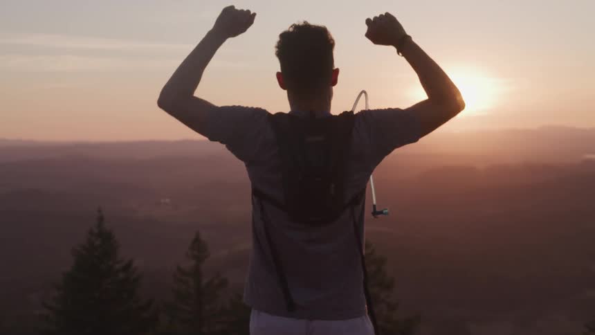 A man celebrates his run up the slope as the sun rises