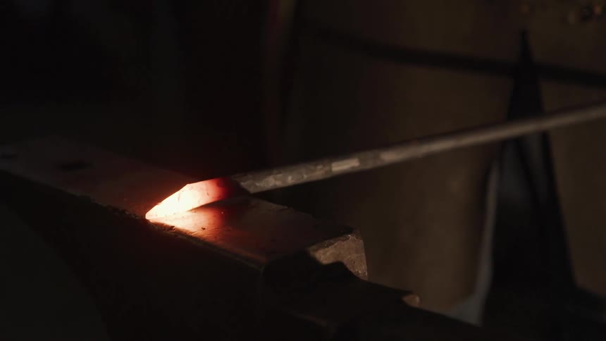 A man hits a hot iron with a hammer and causes sparks to fly