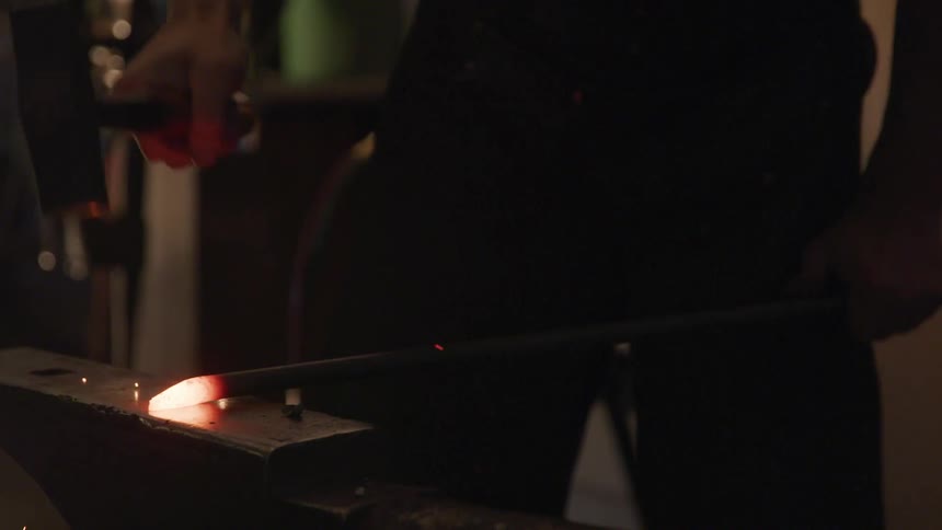 A blacksmith hits the end of heated metal on an anvil