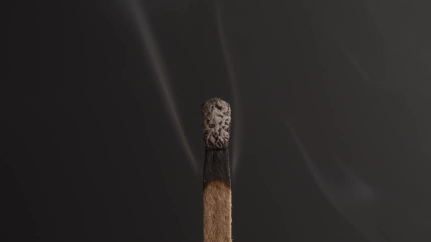 Matchstick burning slowly and then being blown out as smoke rises from the hot surface