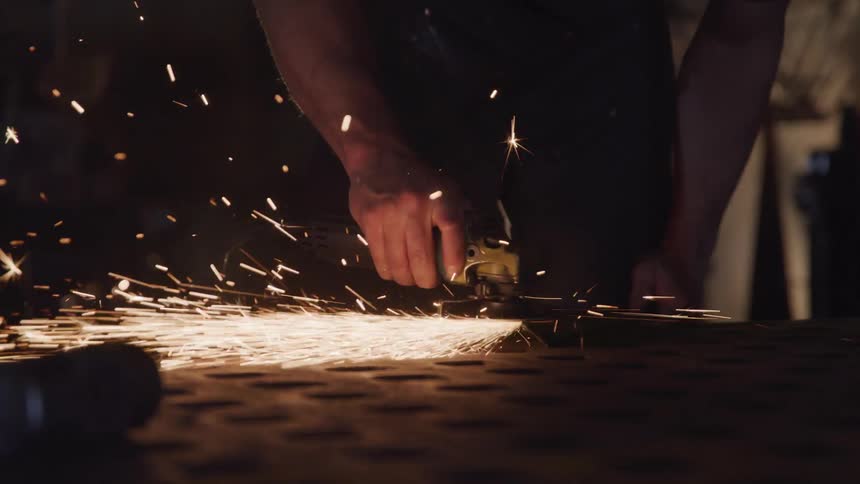 A man uses a mechanical grinder on a piece of metal as sparks shoot outward from it