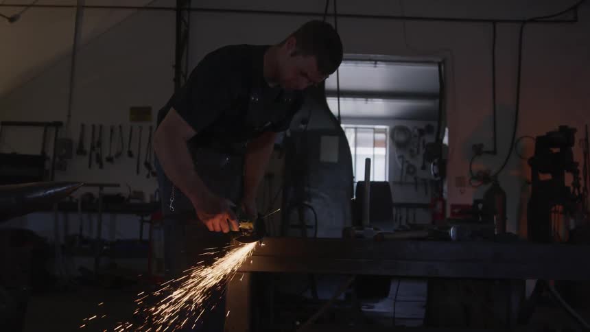 A man uses a grinding wheel on a piece of metal in a workshop