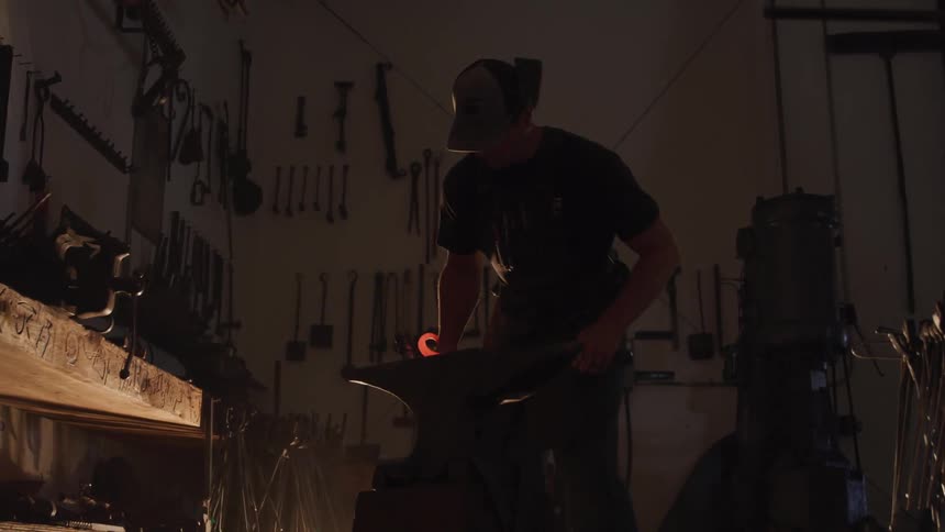 A man hits a piece of hot metal with a hammer on an anvil