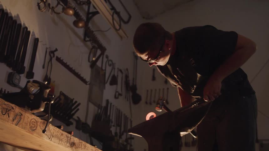 A man uses a hammer and pounds a red hot piece of metal