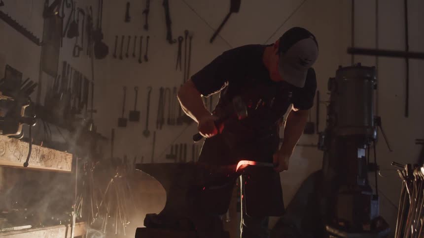 A man hammers red hot heated metal on an anvil