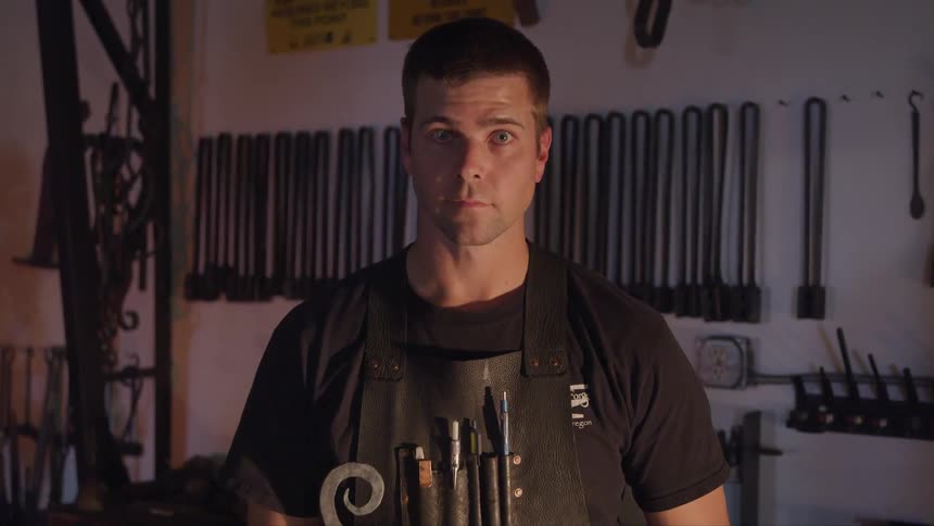 A craftsman in a workshop looks up from his work space and directly at the camera