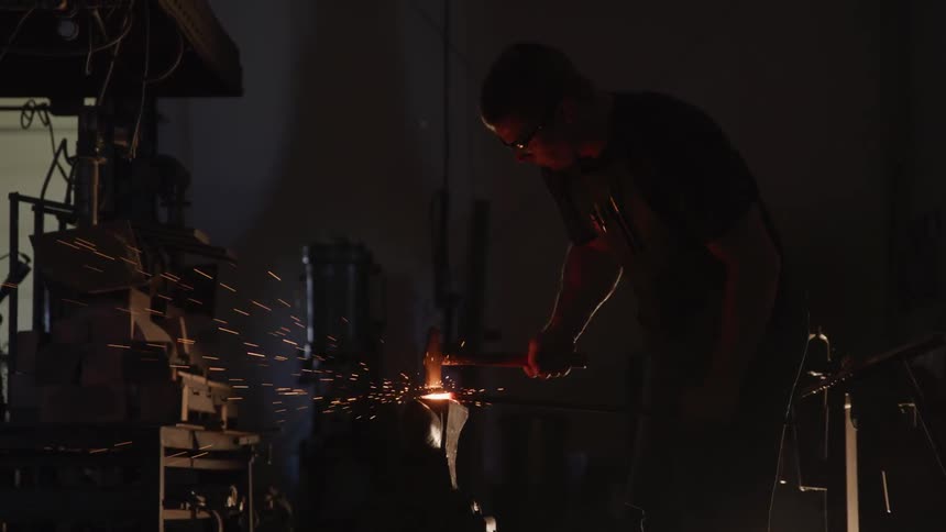 A blacksmith hammers a piece of hot metal on an anvil
