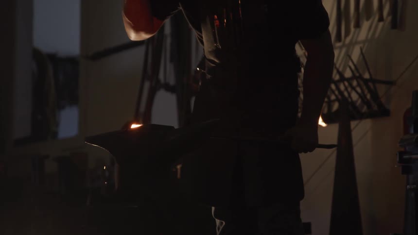 A man uses a hammer on a hot piece of metal