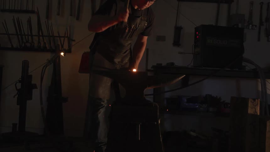 Sparks fly as a man strikes heated metal on an anvil with a hammer