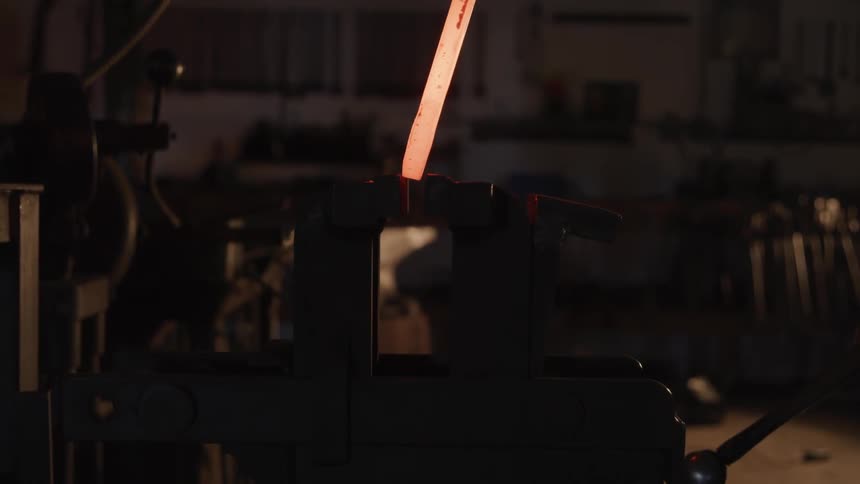 A blacksmith holds a glowing piece of metal and a mallet in a workshop