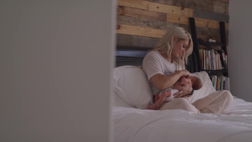 Mother gazing down at her newborn while breastfeeding on her bed