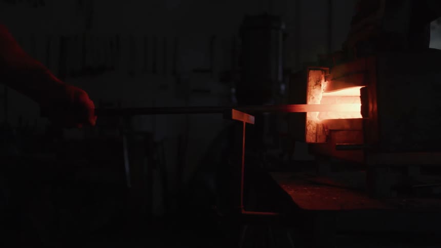 A rod of red hot metal being withdrawn from a forge in a dark room