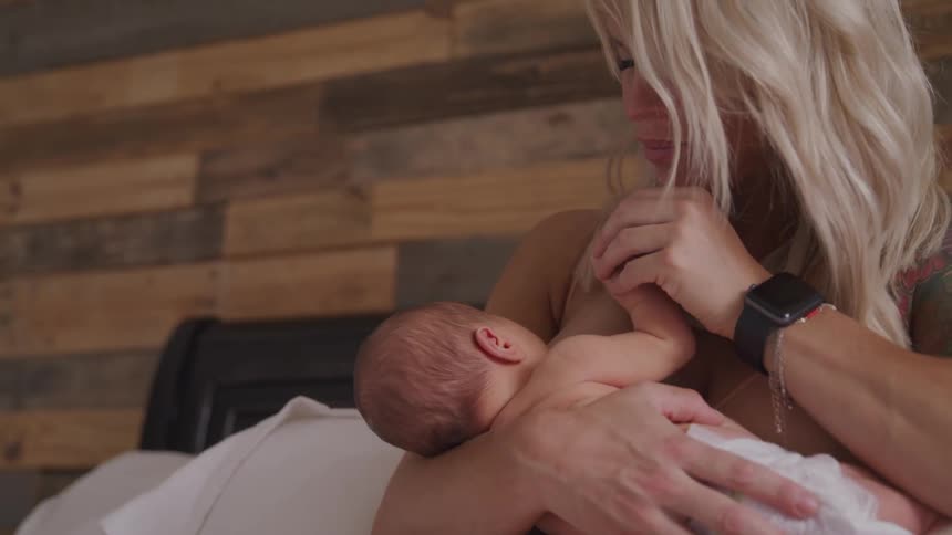 A blonde haired woman kisses the hand of her newborn baby