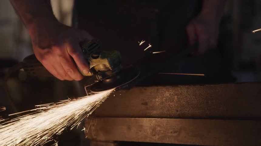 A man uses an angle grinder to grind a piece of metal creating a shower of sparks