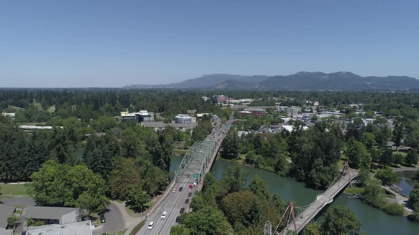 Cars travel on a highway and over a bridge through a business district with lots of trees