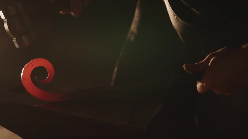 A man shaping hot iron on an anvil with a hammer