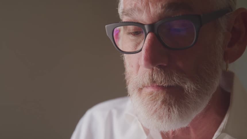 Senior bearded man looks at the typewriter in a room during daylight