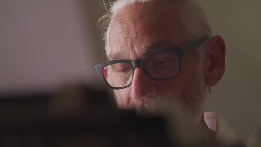 A man looking downward then uses his hand to slide a typewriter