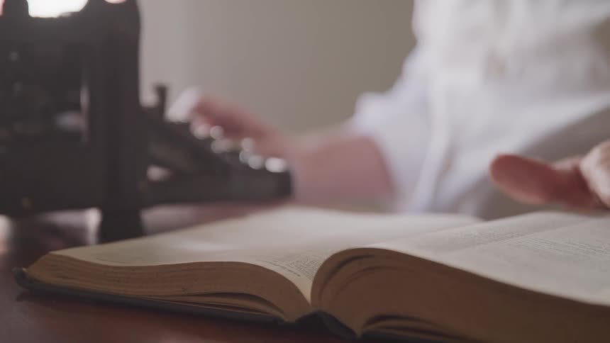 Woman turns the pages of a book then touches a typewriter
