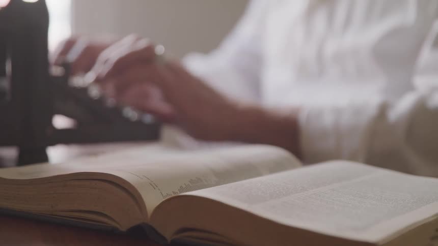 A man typing with a book in front of him