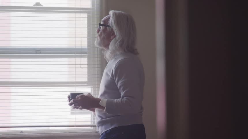 A man holds a mug and stares out a window