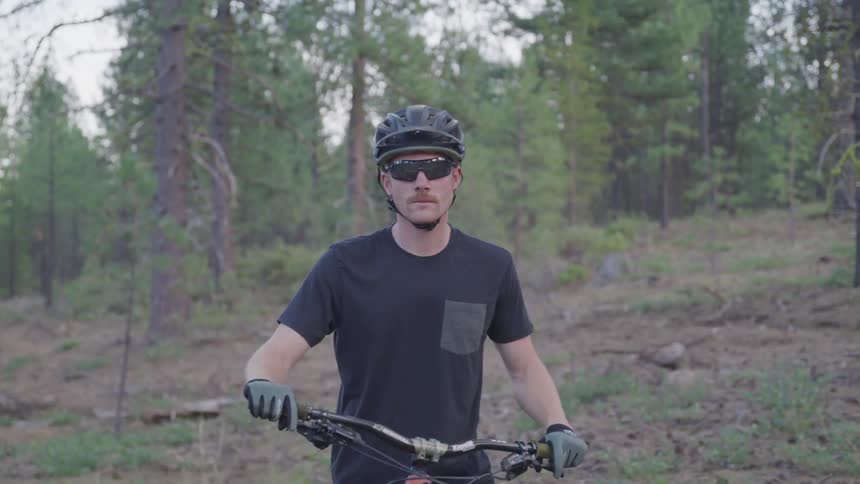Man wearing sunglasses sits on a bicycle near the forest