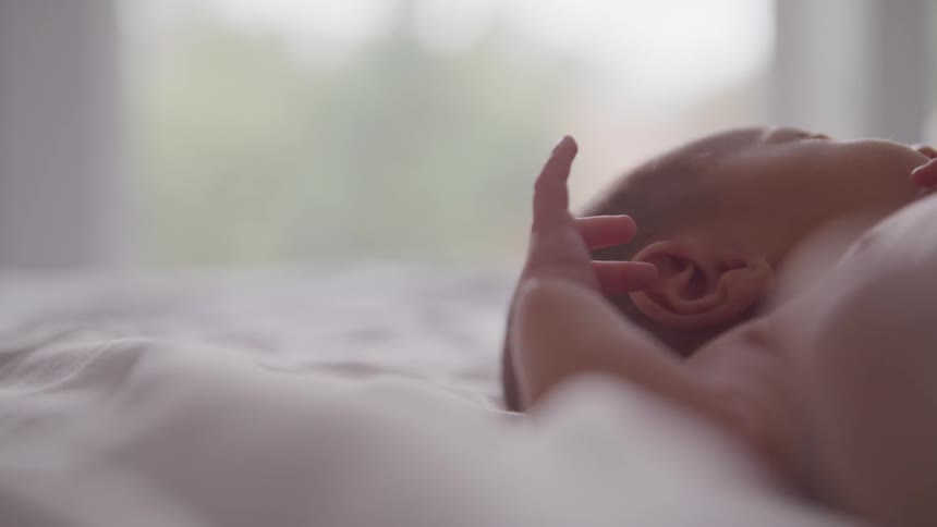 A sleeping infant on a white blanket near a window