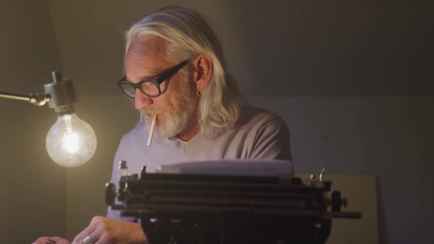 Long grey hair man sitting at the table smokes in a room