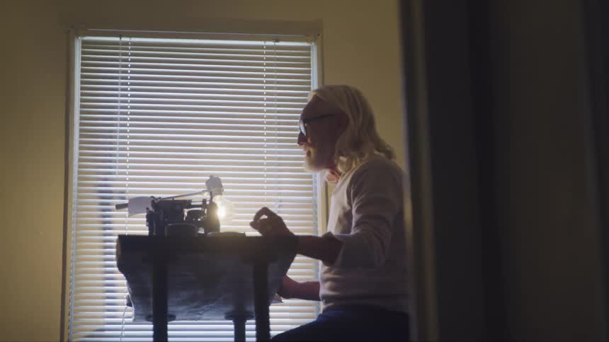 A man sits at his desk and smokes and types on a typewriter