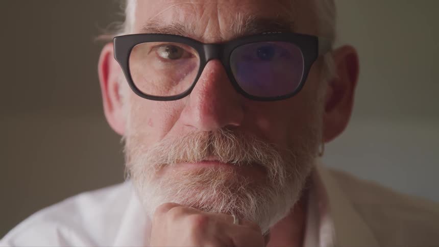 Senior bearded man wearing glasses looks at the camera in a room