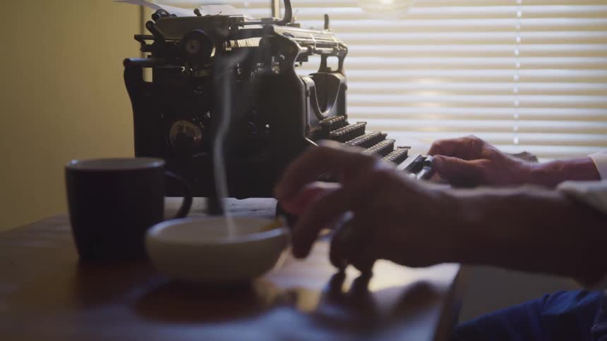 A man smokes a cigarette and types on an old typewriter