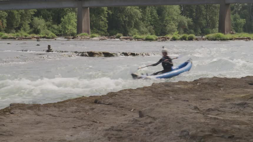 A man in a kayak quickly paddles quickly as he moves swiftly along a rushing river