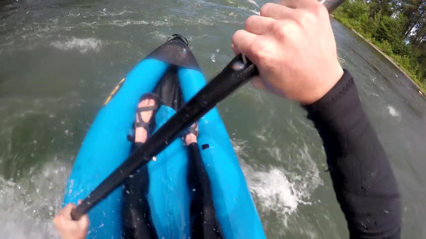A first person perspective shows a man paddling and inflatable kayak over the rapids of a river