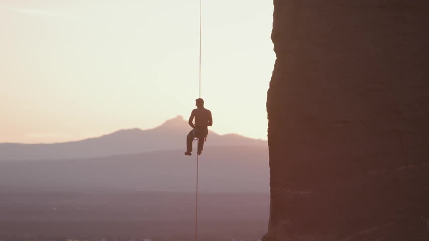 A person lowers themselves down a line that hangs freely beside a rock formation