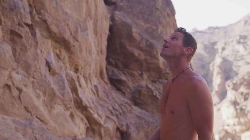 A shirtless man stares up at a mountain