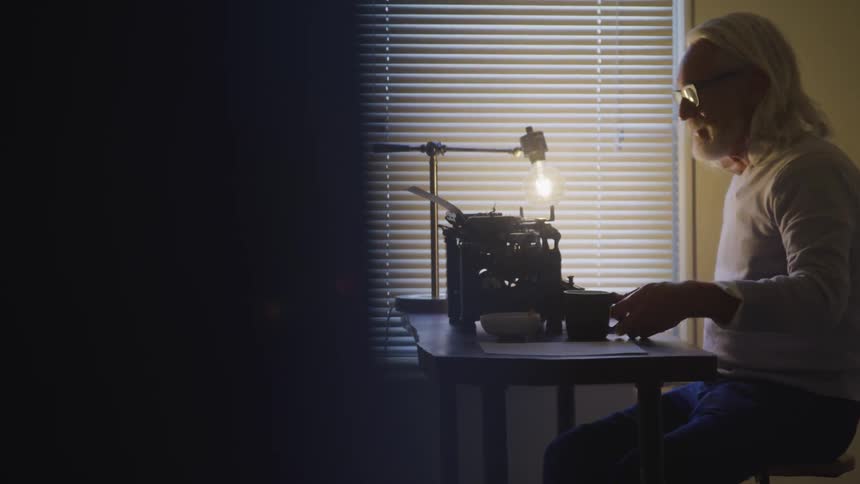 Long grey hair man sitting at the table drinks a cup coffee in a room