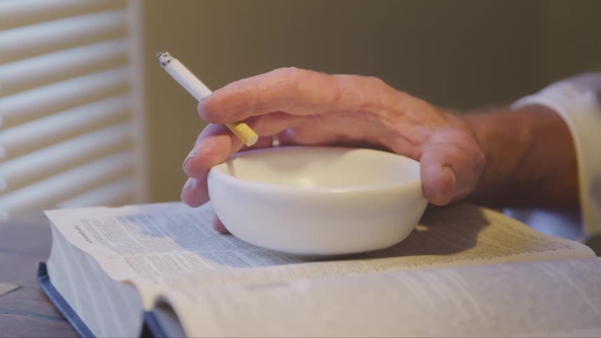 A man with a cigarette holds on to the ashtray bowl sitting on an open book