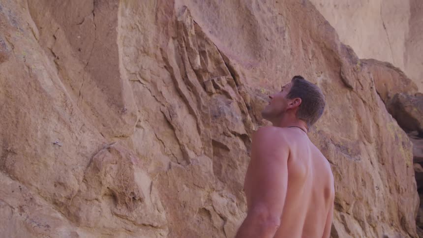 Shirtless rock climber standing in front of cliff