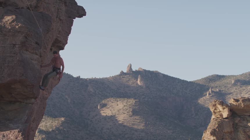 A man is using climbing gear to repel down a rock face with mountains in the background